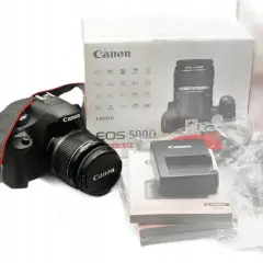 Aparat Canon EOS 500D z obiektywem i akcesoriami na białym tle.