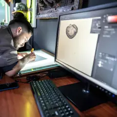 Artysta pracuje przy podświetlanym stole, a na monitorze widać program graficzny. Może szukać informacji, jak zmienić język w Photoshopie.
