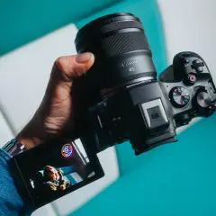 Dłoń trzyma zaawansowany **canon aparat lustrzanka** z obiektywem RF 45mm. Na ekranie widoczny jest podgląd ujęcia.