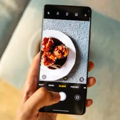 Dłoń trzyma smartfon z widokiem na talerz z ciastkami i sos.