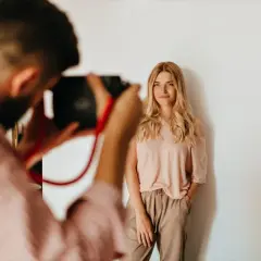 Fotograf robi zdjęcie uśmiechniętej blondynce. Zastanawiasz się, ile kosztuje sesja u fotografa?