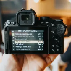 Dłoń trzyma aparat cyfrowy z widocznym menu nagrywania wideo.