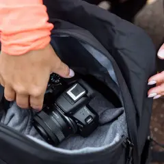 Dłonie wkładają aparat Canon EOS R50 do plecaka. To świetny aparat fotograficzny na początek przygody z fotografią.