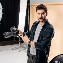 Młody fotograf z aparatem w studio. Chcesz wiedzieć, jak napisać opinie dla fotografa? Oto wskazówki!