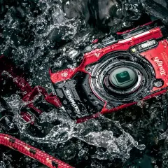 Czerwony, pancerny aparat Olympus Tough w akcji, zanurzony w wodzie. Idealny aparat do zdjęć podwodnych dla poszukiwaczy przygód.