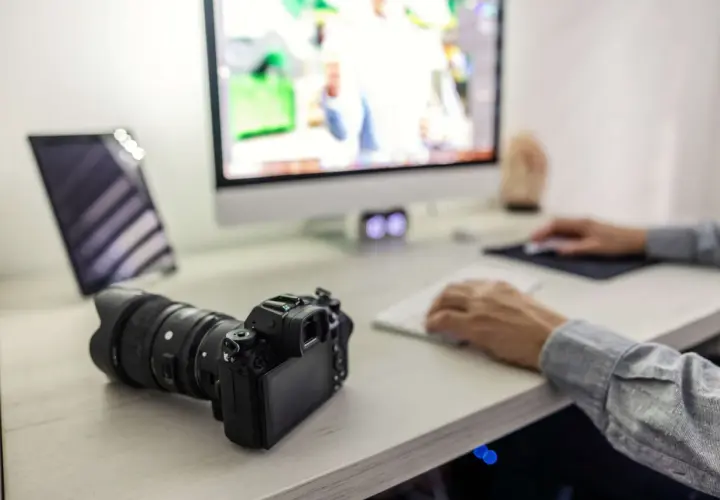 Aparat Sony leży obok komputera, gotowy do zgrania zdjęć. Na ekranie widać edytowane obrazy, a dłonie pracują przy klawiaturze.