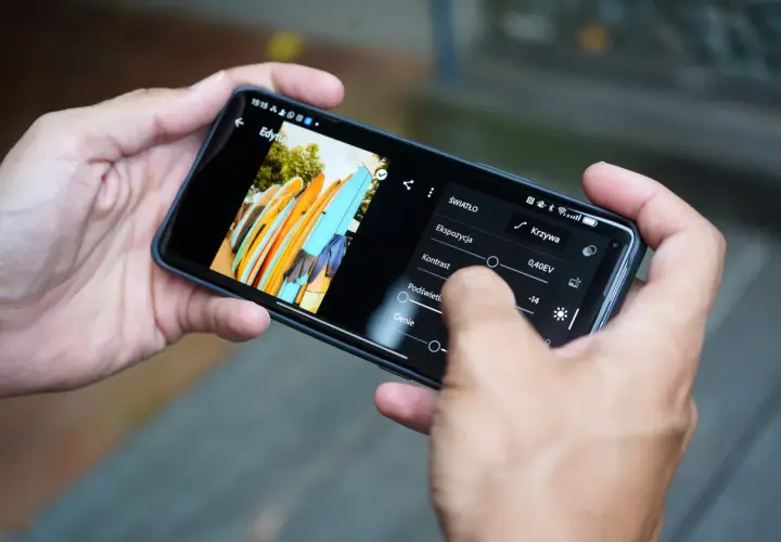 Ręce trzymają smartfon, na którym widać edycję zdjęcia desek surfingowych. Dowiedz się, jak zrobić zdjęcie z filmu na telefonie, edytując je.