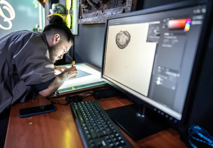 Artysta pracuje przy podświetlanym stole, a na monitorze widać program graficzny. Może szukać informacji, jak zmienić język w Photoshopie.