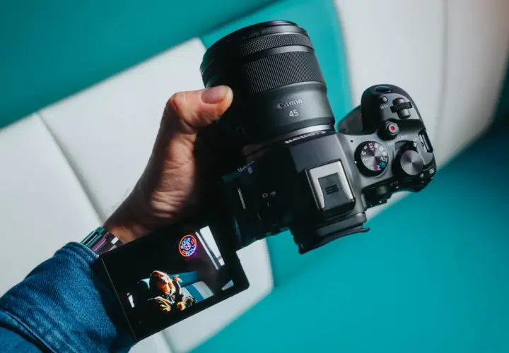 Dłoń trzyma zaawansowany **canon aparat lustrzanka** z obiektywem RF 45mm. Na ekranie widoczny jest podgląd ujęcia.