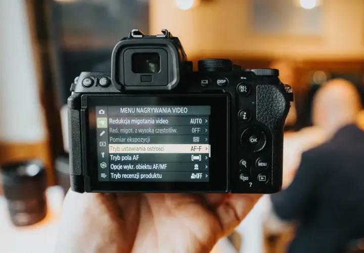 Dłoń trzyma aparat cyfrowy z widocznym menu nagrywania wideo.