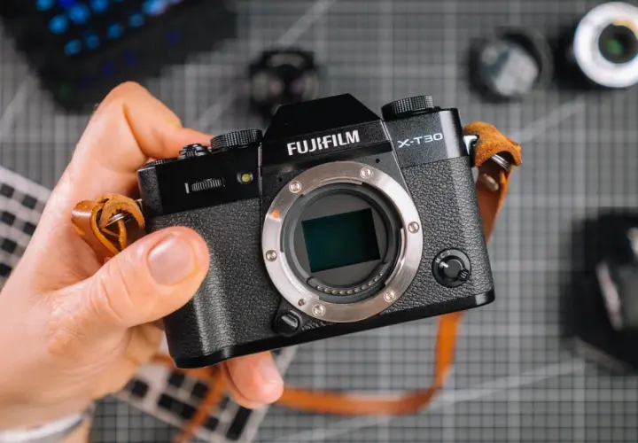 Dłoń trzyma aparat Fujifilm X-T30. Zastanawiasz się, ile kosztuje profesjonalny aparat fotograficzny? Ten model to świetny wybór.