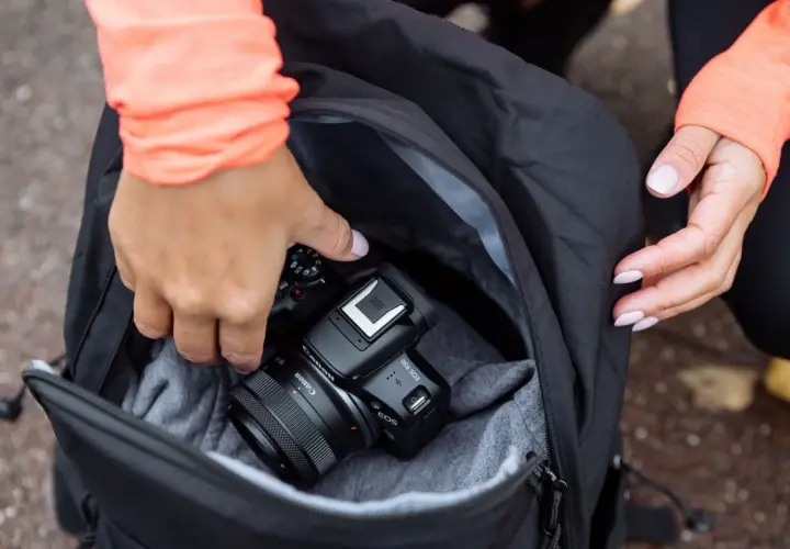 Dłonie wkładają aparat Canon EOS R50 do plecaka. To świetny aparat fotograficzny na początek przygody z fotografią.