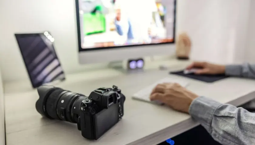Aparat Sony leży obok komputera, gotowy do zgrania zdjęć. Na ekranie widać edytowane obrazy, a dłonie pracują przy klawiaturze.