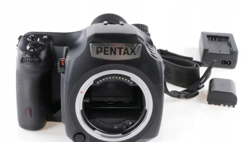 Czarna lustrzanka cyfrowa Pentax z paskiem i akcesoriami, gotowa do aukcji na Allegro.
