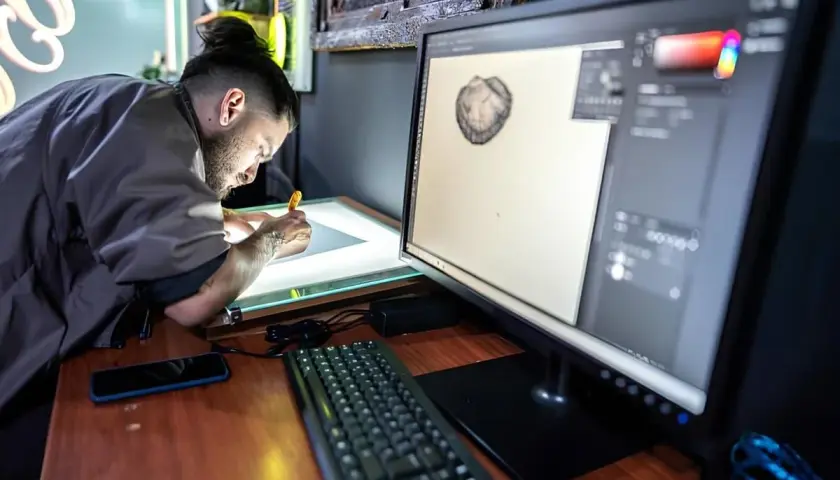 Artysta pracuje przy podświetlanym stole, a na monitorze widać program graficzny. Może szukać informacji, jak zmienić język w Photoshopie.