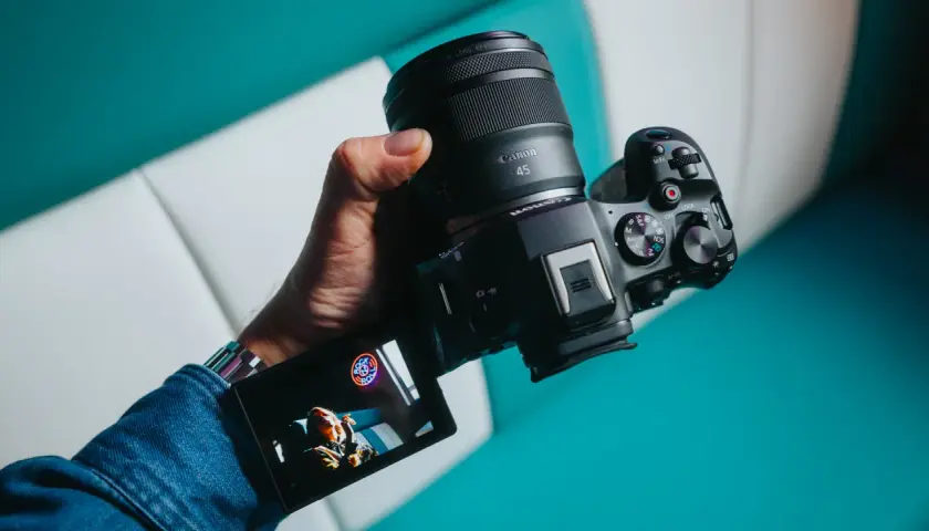 Dłoń trzyma zaawansowany **canon aparat lustrzanka** z obiektywem RF 45mm. Na ekranie widoczny jest podgląd ujęcia.