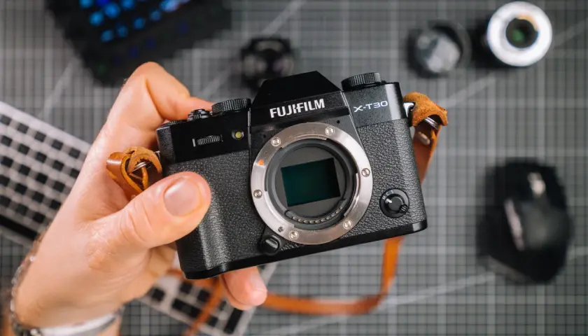 Dłoń trzyma aparat Fujifilm X-T30. Zastanawiasz się, ile kosztuje profesjonalny aparat fotograficzny? Ten model to świetny wybór.