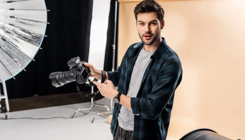 Młody fotograf z aparatem w studio. Chcesz wiedzieć, jak napisać opinie dla fotografa? Oto wskazówki!