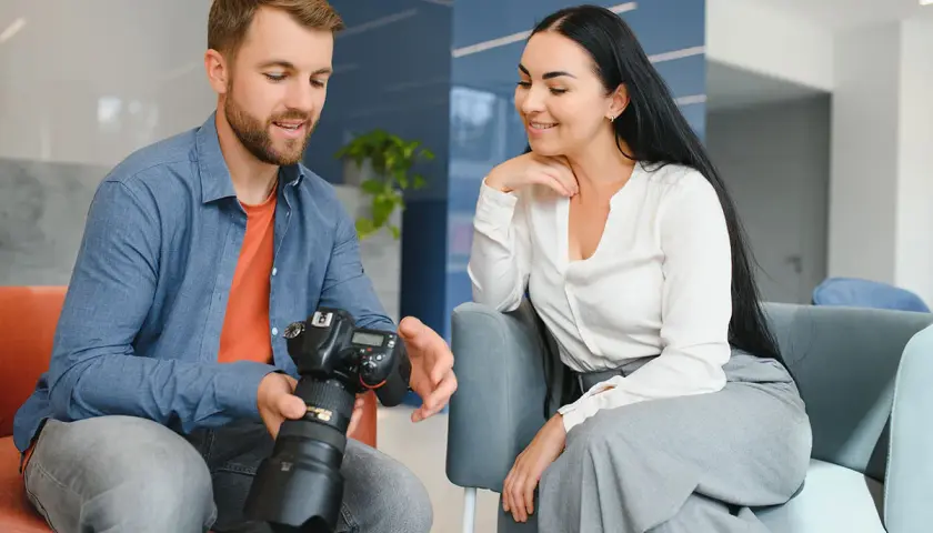 Mężczyzna z aparatem pokazuje kobiecie efekty swojej pracy. Fotograf omawia szczegóły sesji.