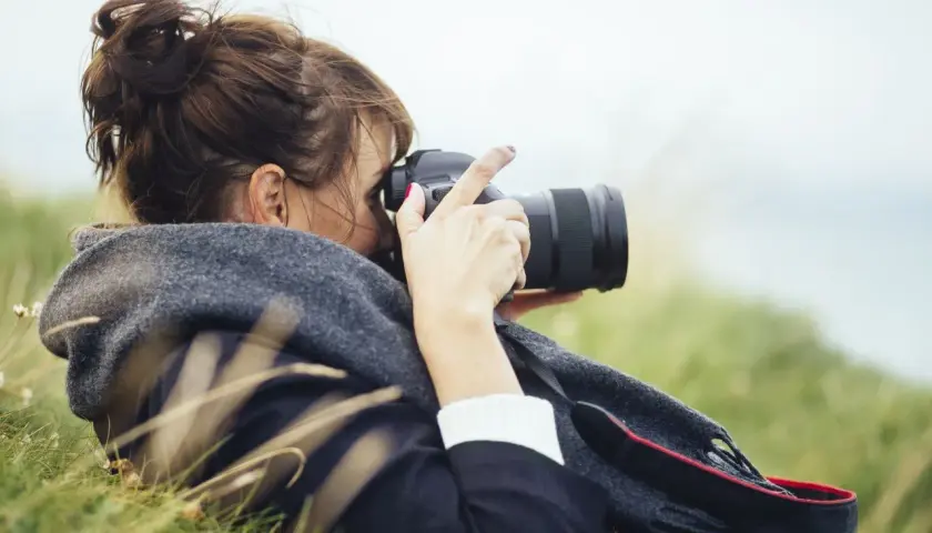 Kobieta z włosami spiętymi w kok leży na trawie, robiąc zdjęcie profesjonalną lustrzanką do vlogów.