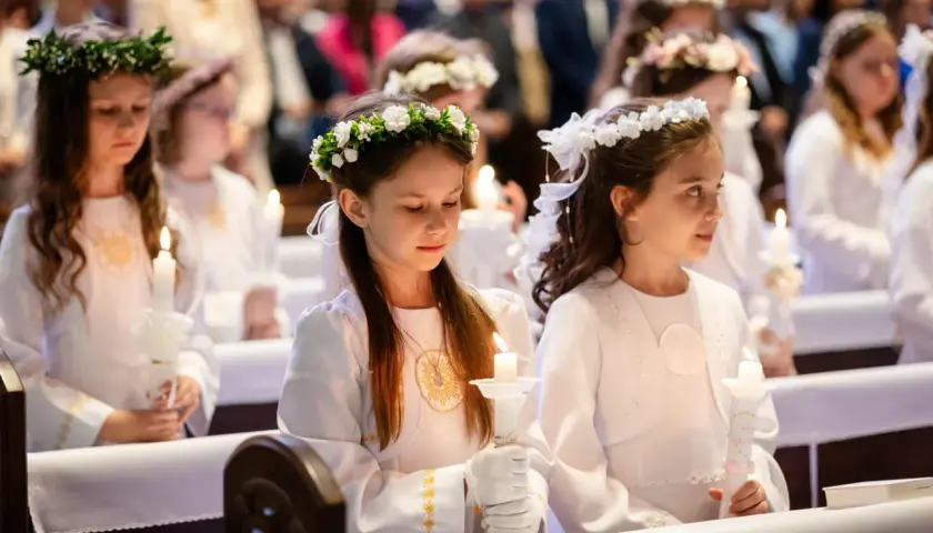 Dziewczynki w białych strojach z wiankami na głowach trzymają świece. Zastanawiasz się, ile kosztuje fotograf na komunie?