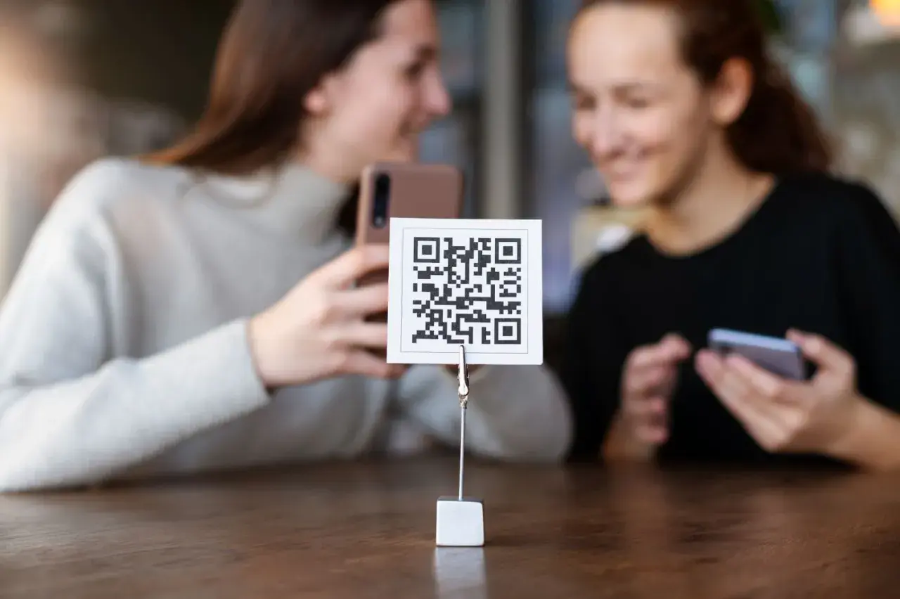 Dwie dziewczyny próbują zeskanować kod QR aparatem telefonu. Proste jak budowa cepa!