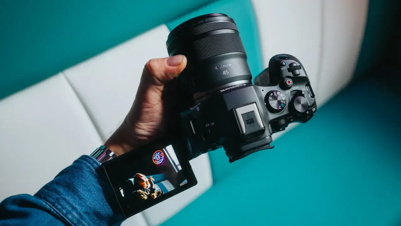 Dłoń trzyma zaawansowany **canon aparat lustrzanka** z obiektywem RF 45mm. Na ekranie widoczny jest podgląd ujęcia.