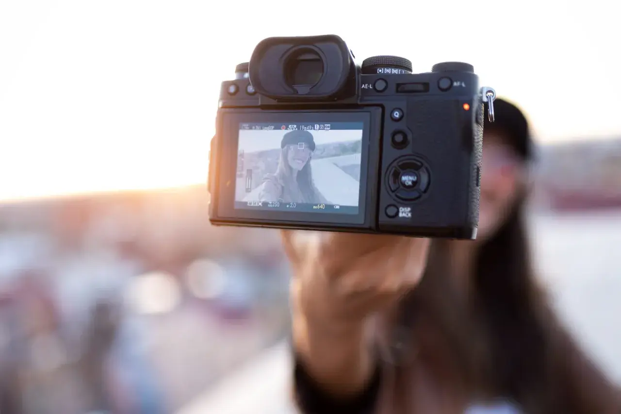 Aparat fotograficzny trzymany przez rękę, na ekranie selfie uśmiechniętej kobiety.
