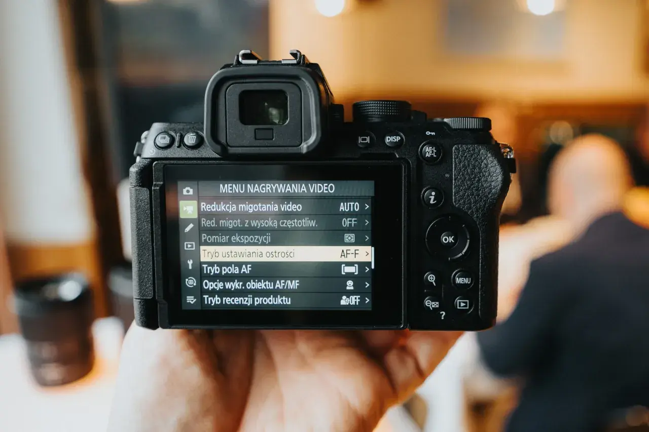 Dłoń trzyma aparat cyfrowy z widocznym menu nagrywania wideo.