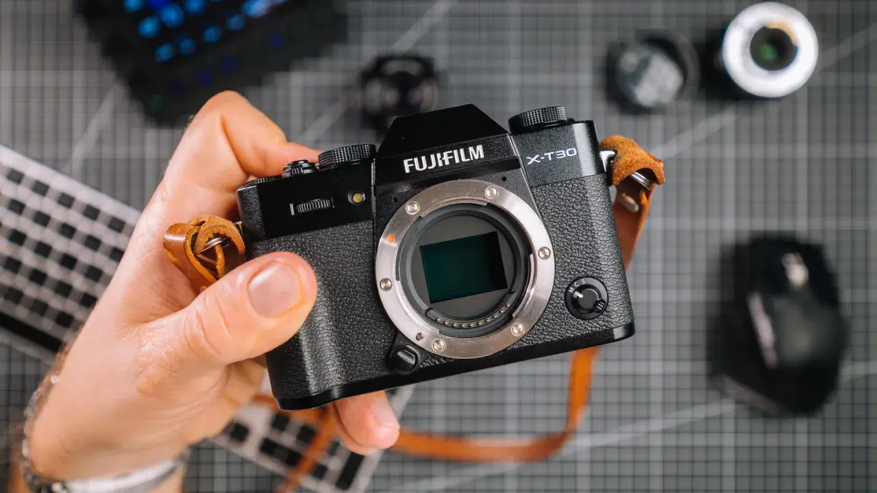 Dłoń trzyma aparat Fujifilm X-T30. Zastanawiasz się, ile kosztuje profesjonalny aparat fotograficzny? Ten model to świetny wybór.