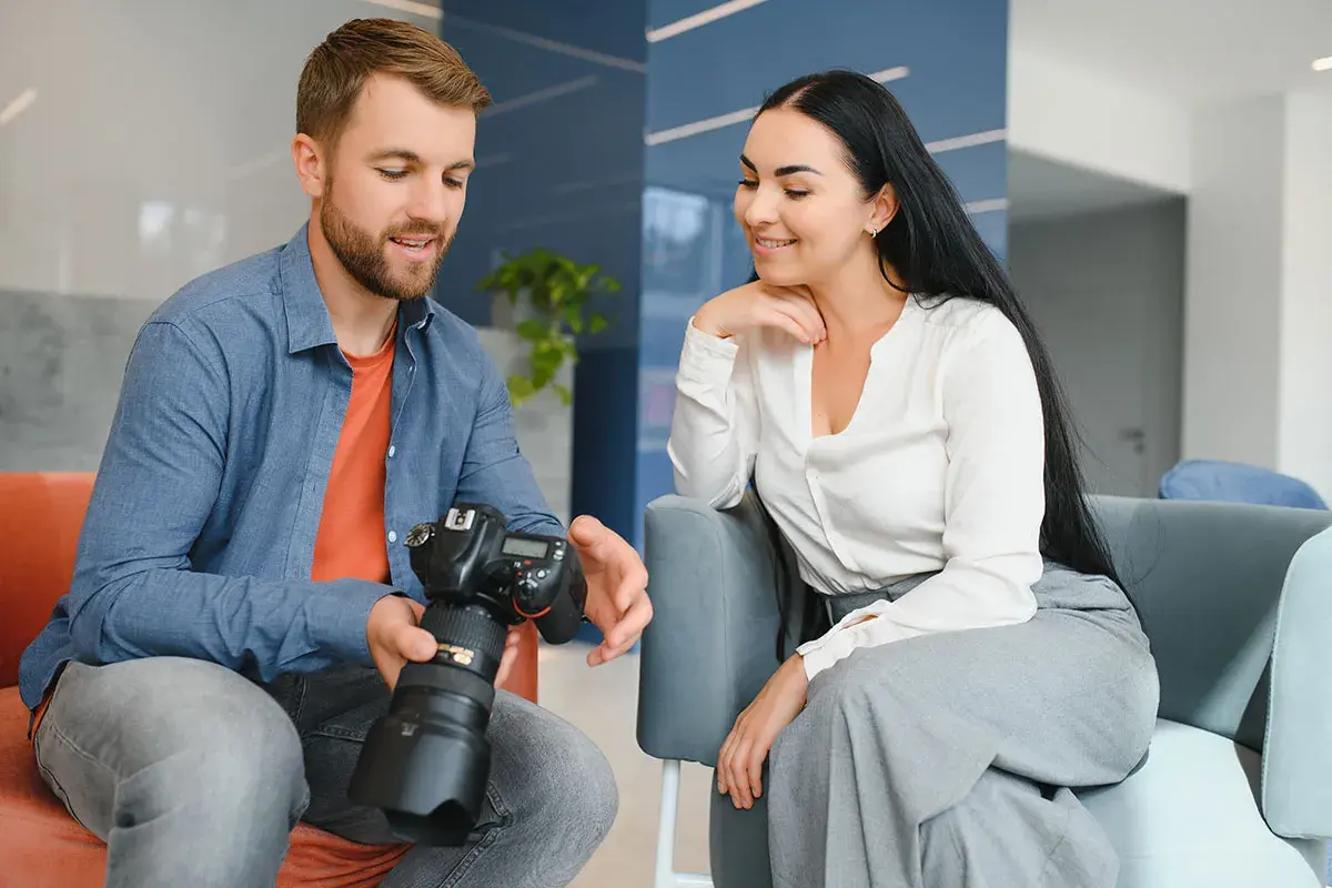 Mężczyzna z aparatem pokazuje kobiecie efekty swojej pracy. Fotograf omawia szczegóły sesji.