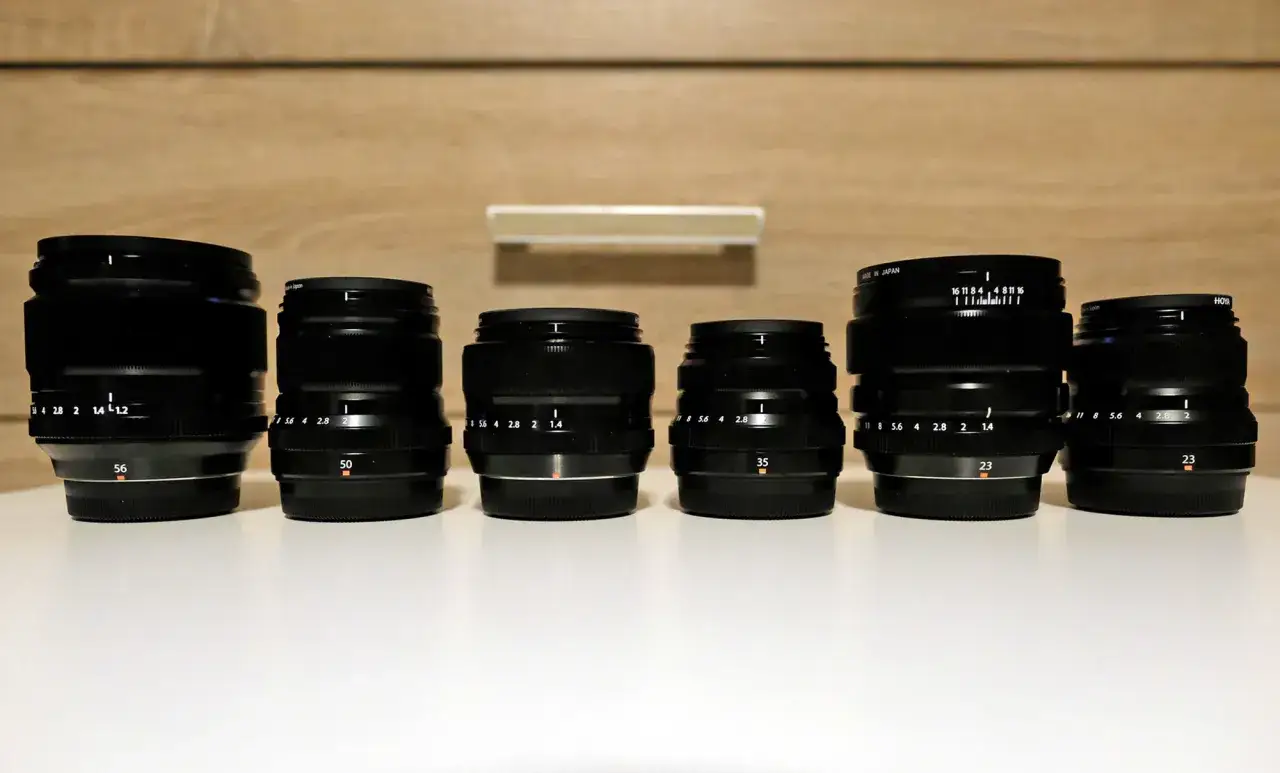 Sześć obiektywów do aparatu Fujifilm lustrzanka, ustawionych w rzędzie na białej powierzchni.