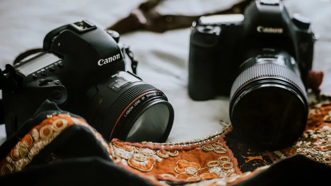 Dwie czarne lustrzanki Canon leżą obok siebie. Jedna z nich ma obiektyw 50mm f/1.2. Różnica między lustrzanką a bezlusterkowcem jest widoczna w ich budowie.