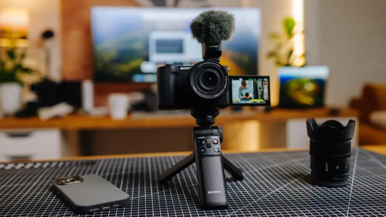 Sony Alpha z mikrofonem i uchwytem na statywie to idealny aparat do filmowania. Obok leży obiektyw i etui na telefon.