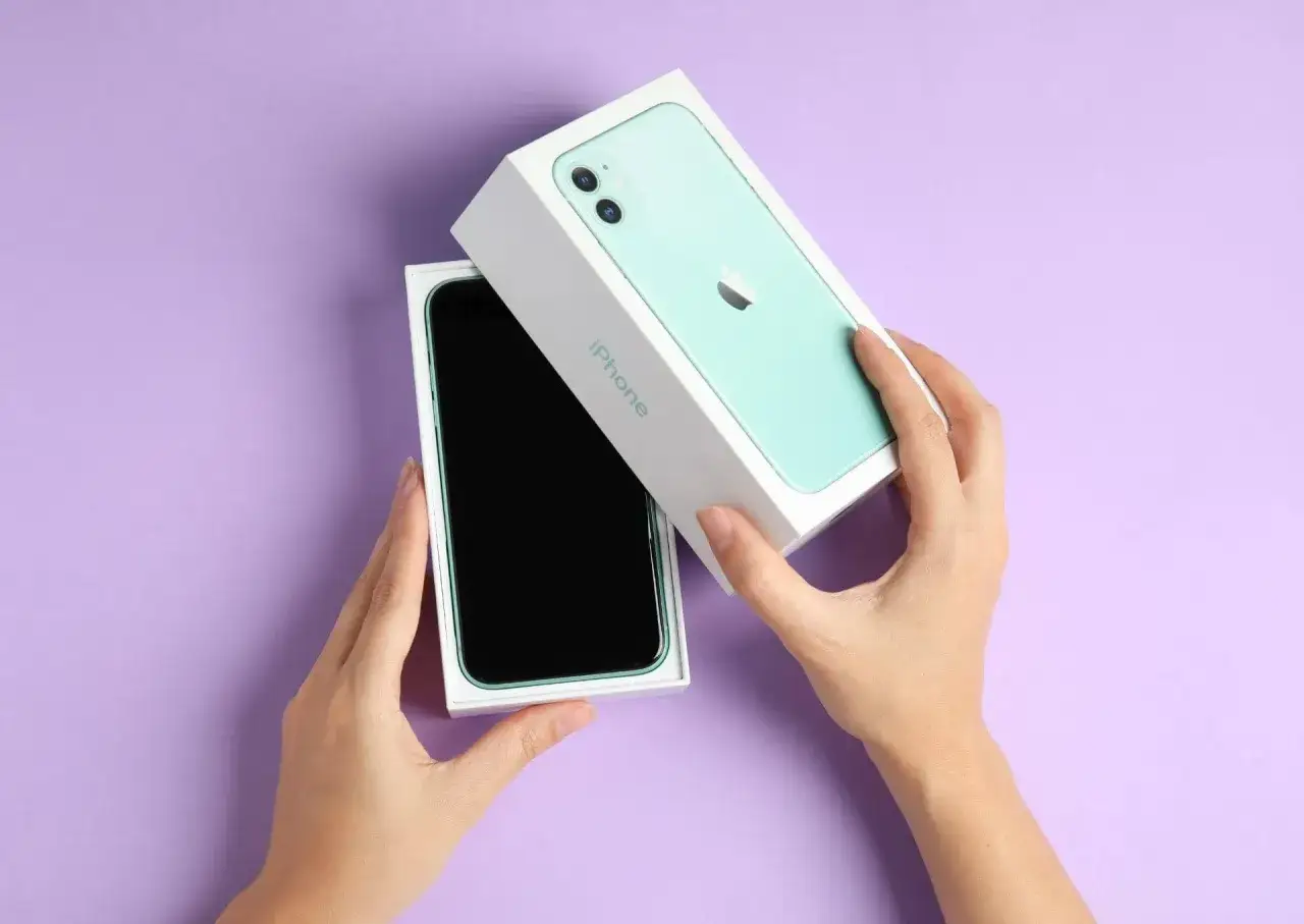 Ręce rozpakowują zielony iPhone 11. Aparat tego modelu pozwala robić świetne zdjęcia.
