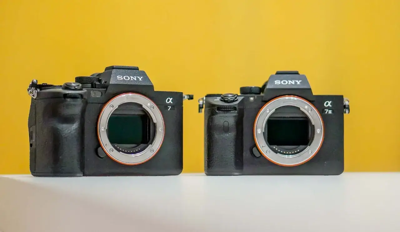 Dwa aparaty Sony Alpha, lustrzanki cyfrowe, stoją obok siebie na białej powierzchni.
