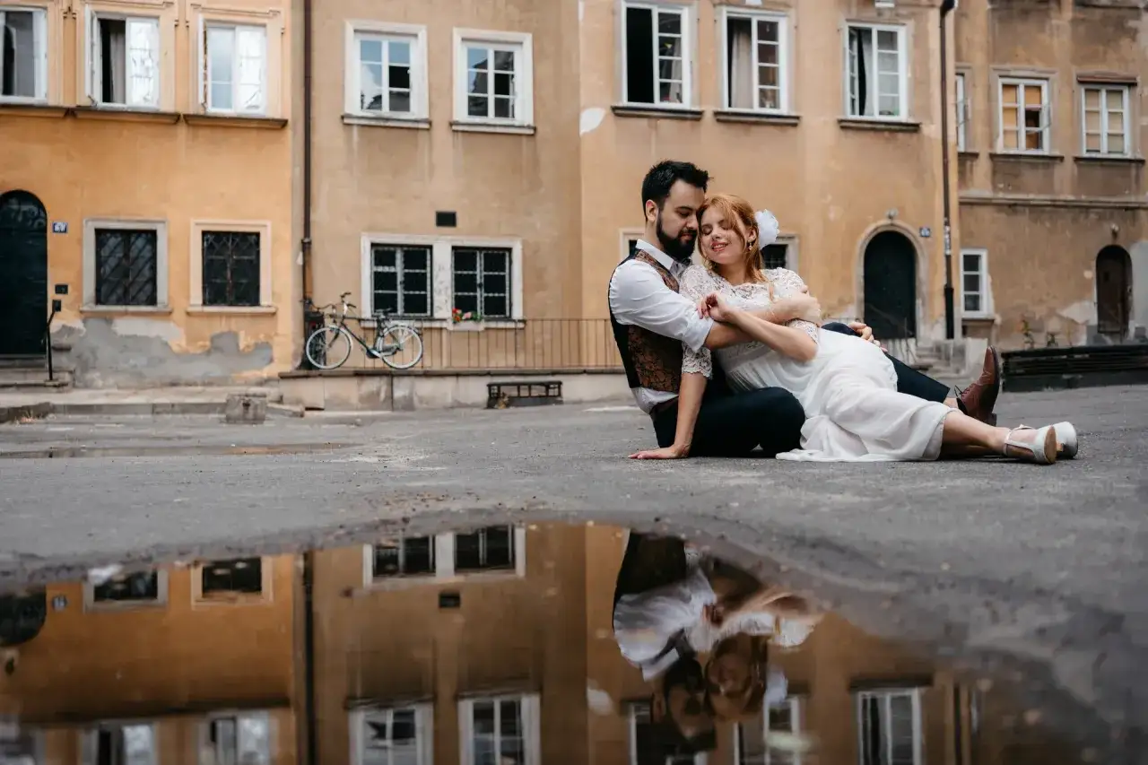 Para wybrać fotografa na wesele, warto zwrócić uwagę na jego styl i portfolio. Para młoda siedzi przytulona na tle kamienicy.