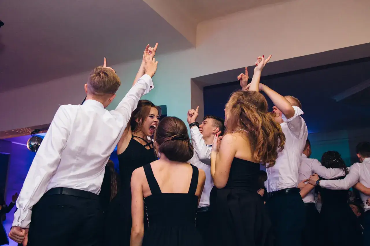 Młodzi ludzie tańczą na studniówce, radośnie unosząc ręce. Zastanawiasz się, ile kosztuje fotograf na studniówkę, by uwiecznić takie chwile?