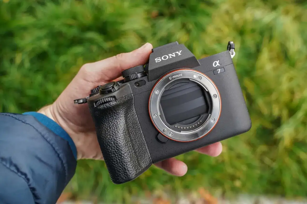 Dłoń trzyma aparat lustrzankę Sony Alpha 7 z obiektywem E-mount.