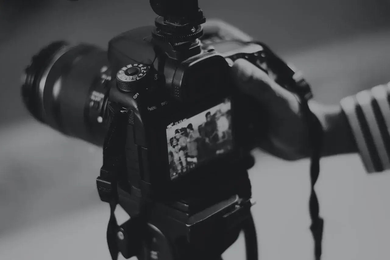 Dłoń trzyma aparat, na ekranie widać ludzi. Zastanawiasz się, ile trwa wywołanie zdjęć u fotografa?
