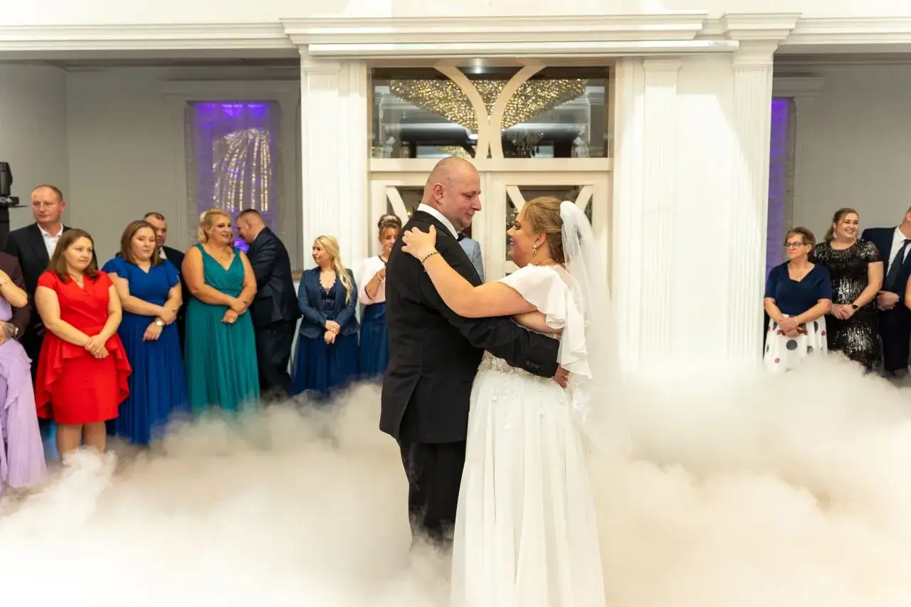 Para imprezy na które wynajmujemy fotografa: para młoda tańczy w chmurach dymu, goście weselni obserwują.