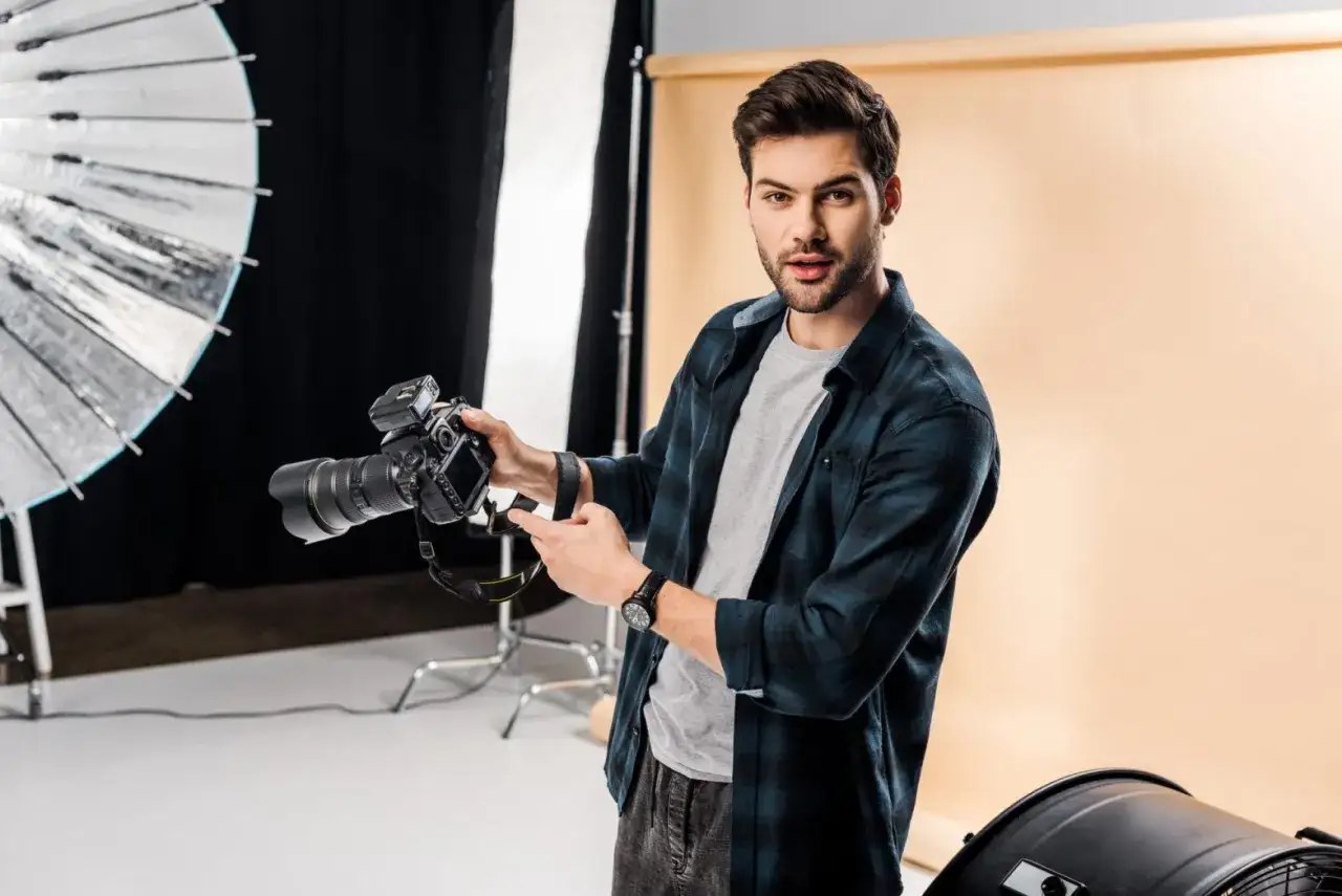 Młody fotograf w studio, trzymający aparat. Chcesz wiedzieć, jak napisać opinie dla fotografa?