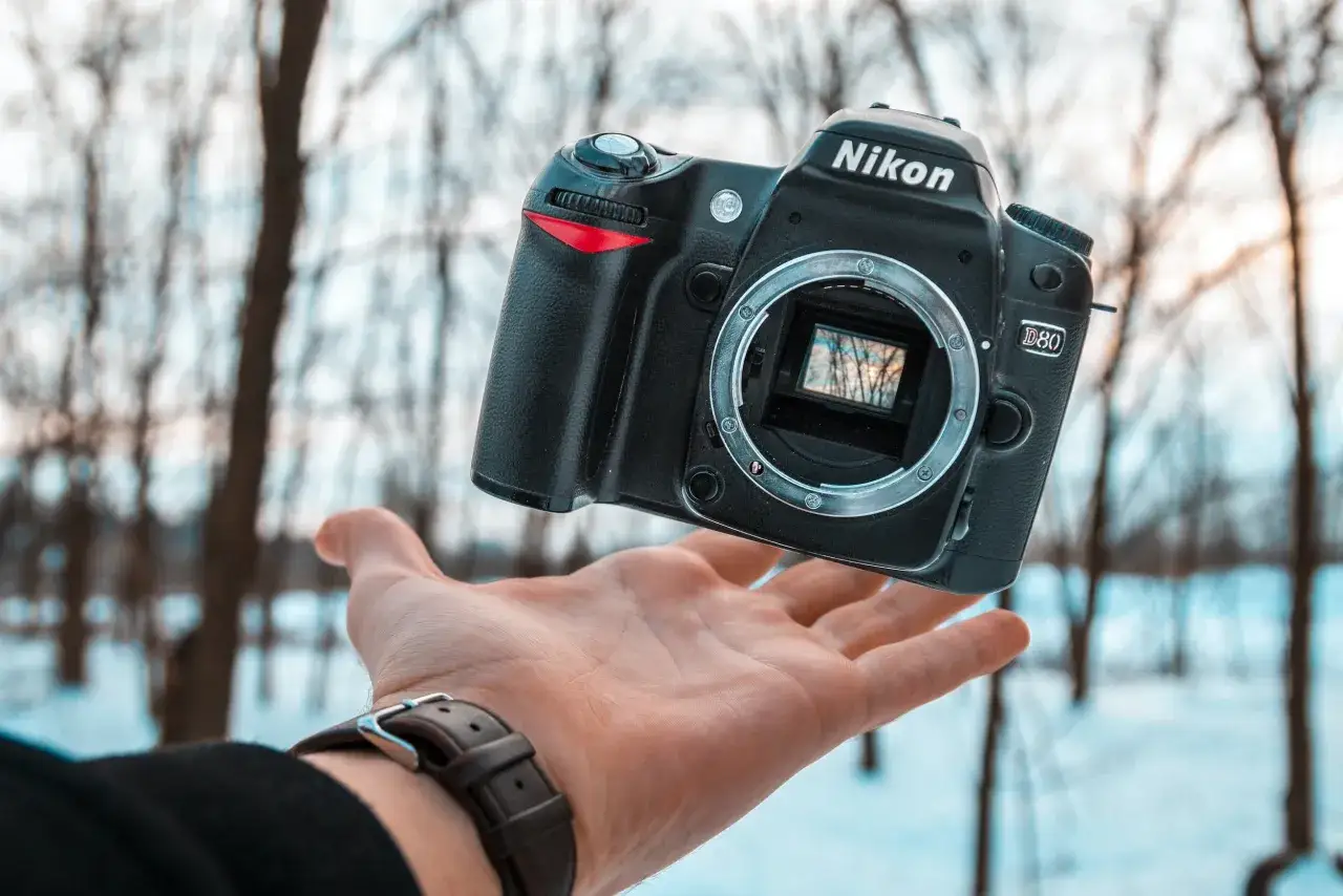 Nikon D80 w dłoni, idealny aparat dla początkujących. Zimowy krajobraz w tle.